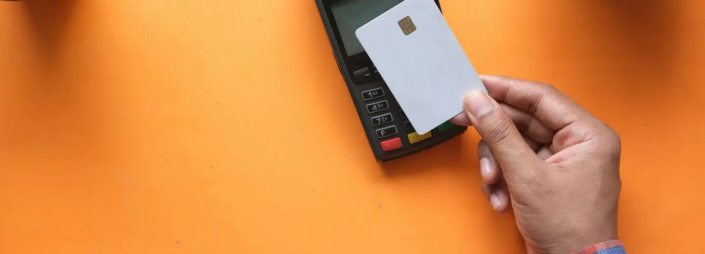 A hand inserting a blank chip card into a black payment terminal on an orange desk
