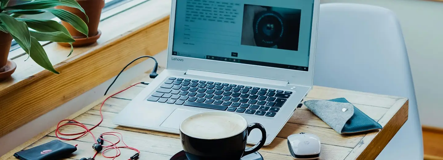 Coffee, laptop and earphones on a warm wooden café table
