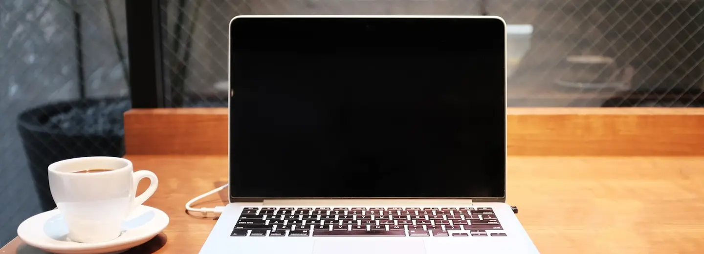 Laptop and a cup of coffee on a wooden desk in morning light