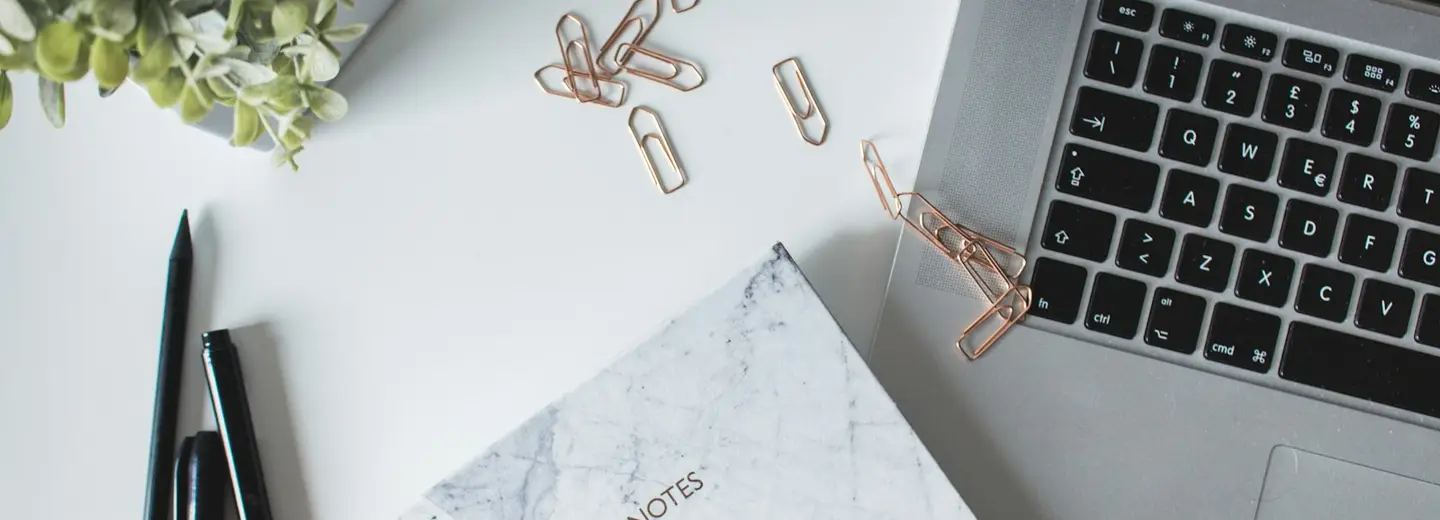 Notebook, laptop and paper clips on a tidy white desk