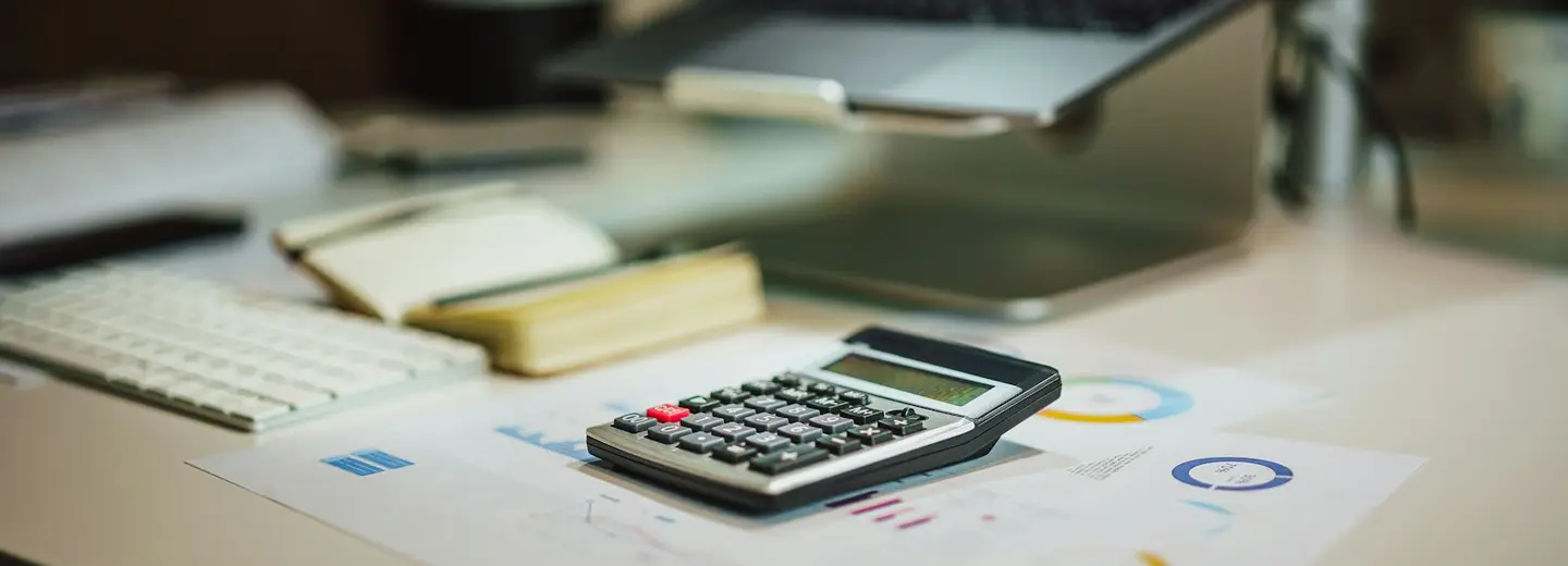 Calculator and notes next to a laptop on a desk