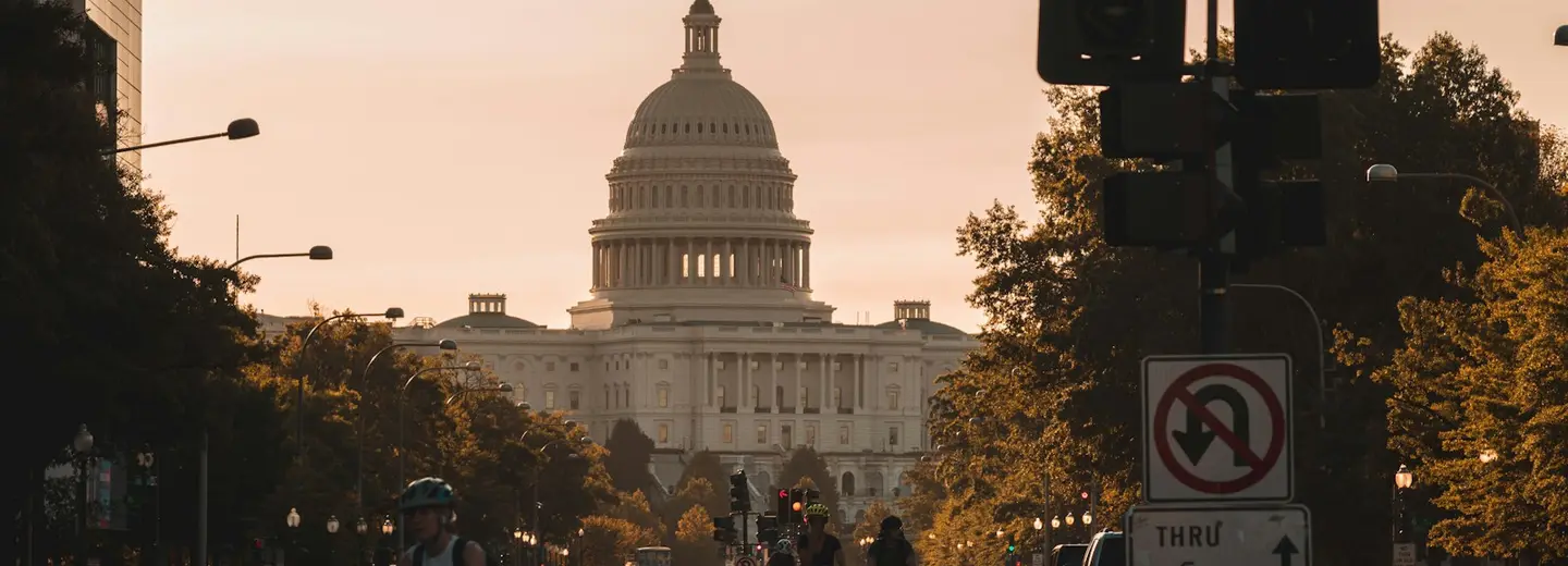 The United States Capitol at the end of a tree-lined avenue, cyclists and traffic in the foreground