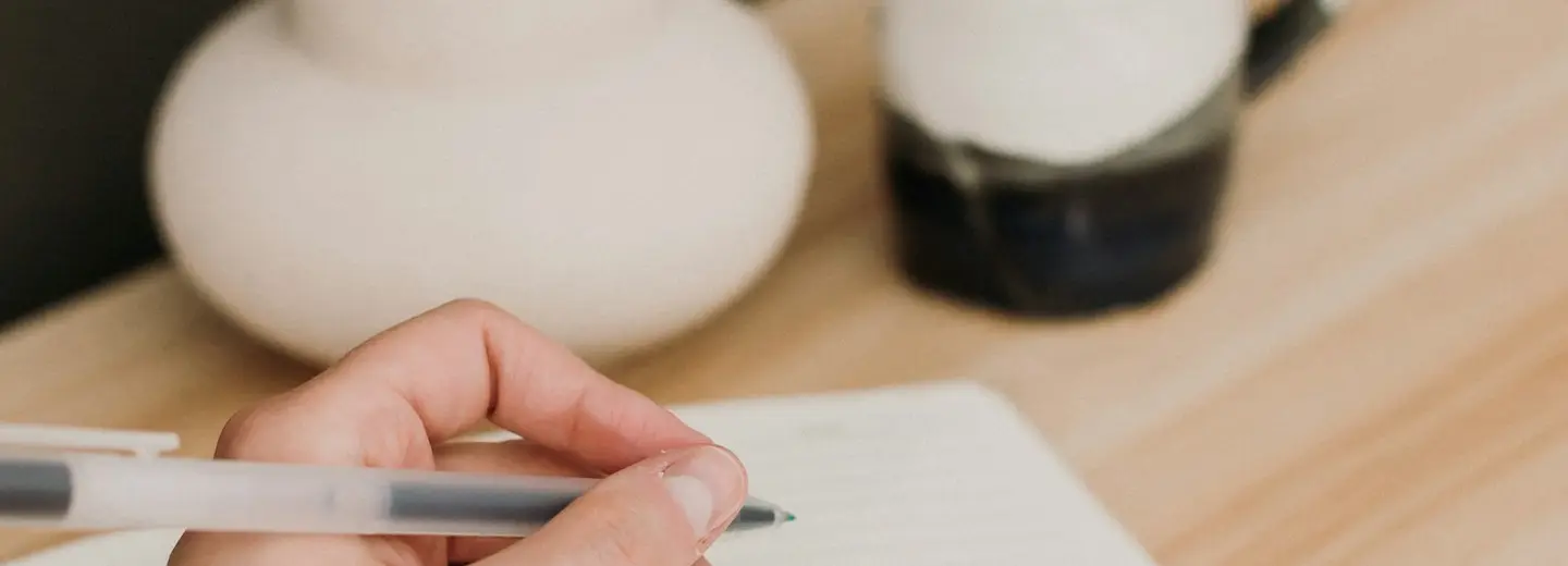 Hand writing in a blank notebook next to a coffee cup