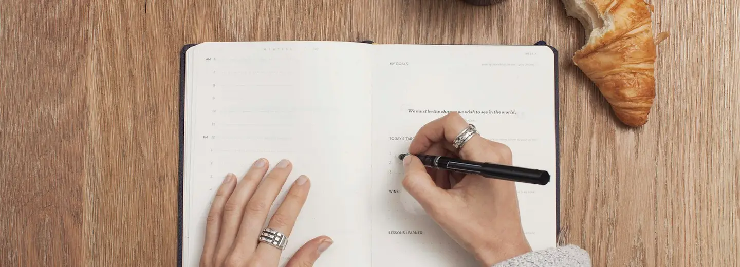 Hands writing in an open journal beside a cup of coffee