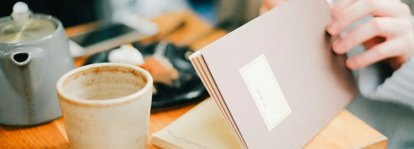 Notebook and teapot on a warm wooden café table