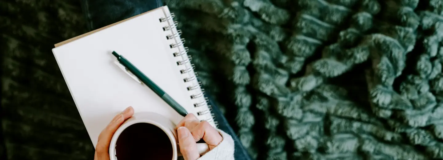 Hands holding a coffee over a notebook ready to start