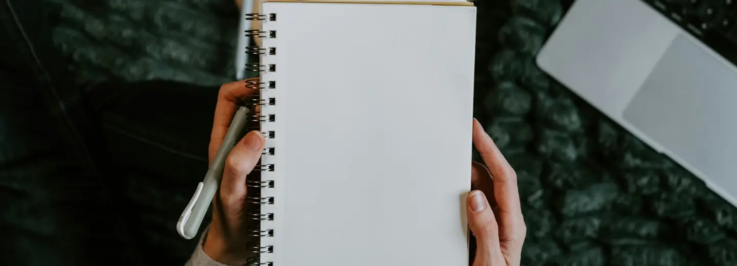 Hands holding an open blank notebook over a desk with coffee